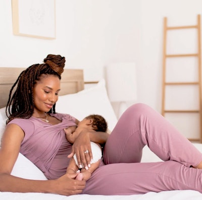 Woman wearing mauve pajamas, laying in bed nursing baby