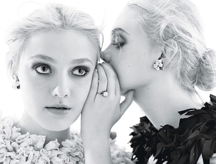 A blonde girl wearing a black feathery collar while whispering in the ear of another blonde girl wea...