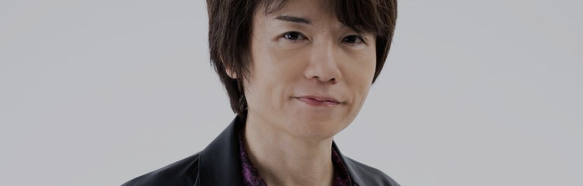 Image of Masahiro Sakurai with short brown hair wearing black leather blazer and maroon button-up sh...