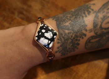 A close-up of a tattooed wrist wearing a black and rose gold Ivy fitness tracker
