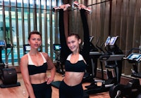 Bella Hadid and her fitness trainer posing at the gym, as Bella lifts weights