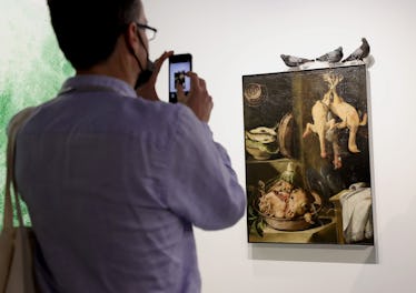A fairgoer taking a photo of a painting with part of Maurizio Cattelan's installation Ghosts at Art ...