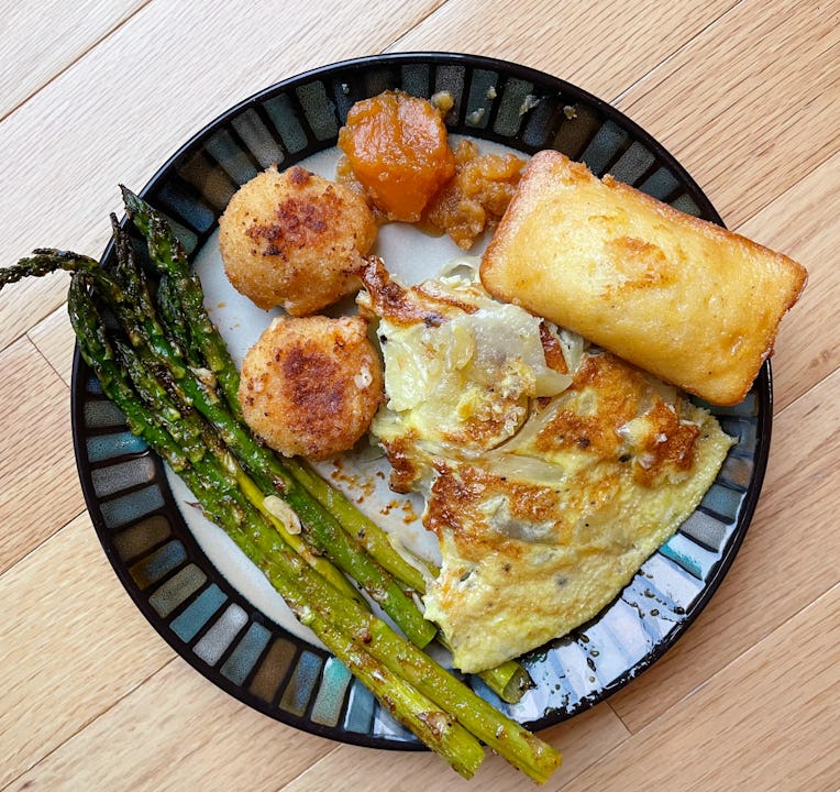 Top-down photo of a plate with roasted asparagus, a Spanish tortilla piece, mac and cheese bites, co...