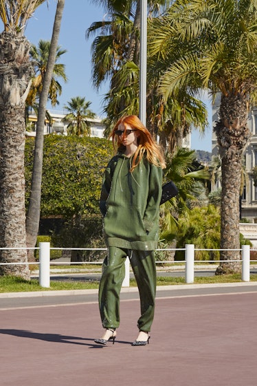 A female model with orange hair walking while wearing a green tracksuit and heels