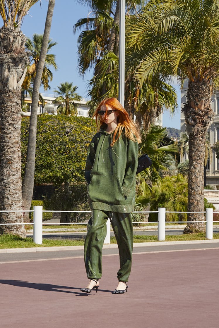 A female model with orange hair walking while wearing a green tracksuit and heels
