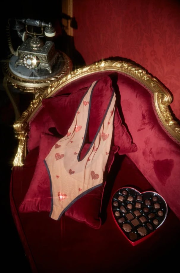 One-piece lingerie bodysuit with crystal hearts, laying on velvet sofa