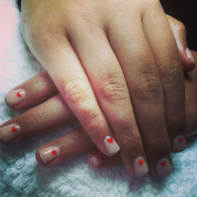 Manicure; nails painted with shimmery/pearl polish and a red heart