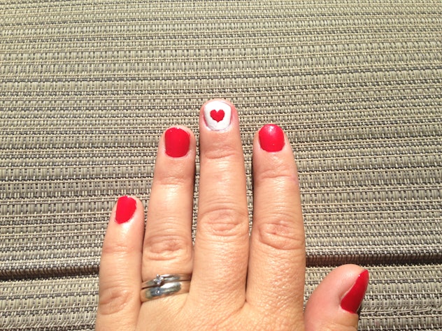Manicure; red nails except middle finger, which is white with red heart