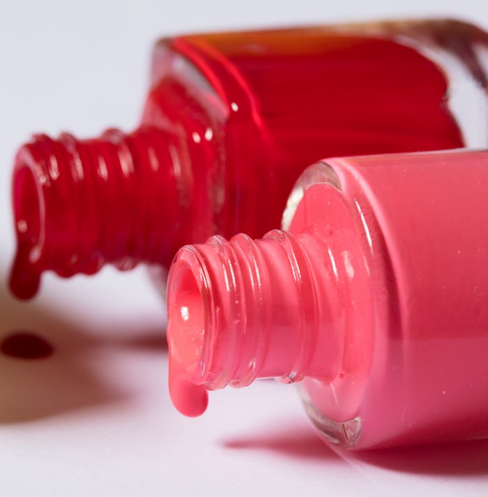 Two bottles of nail polish on their sides dripping; pink and red