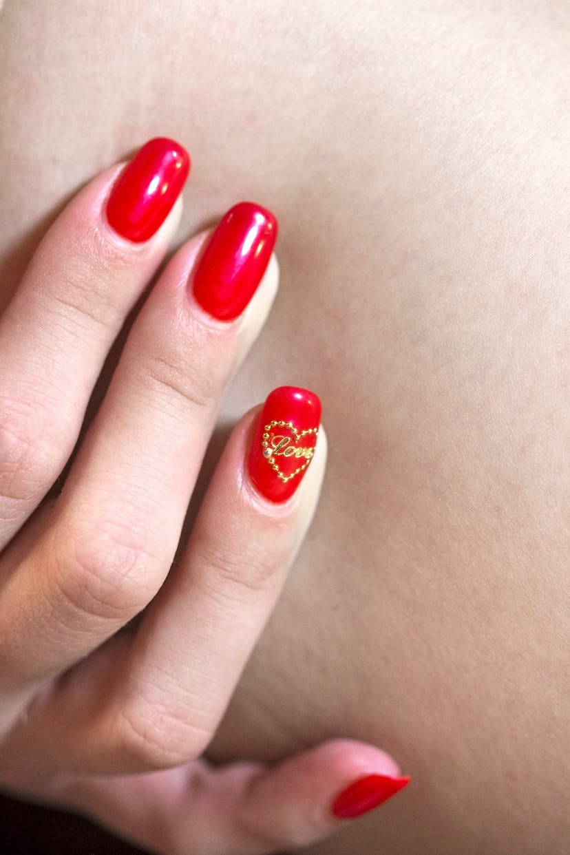 Manicured nails painted red with "love" sticker on ring finger