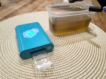 tCheck device is pictured with a test slide inserted, beside a tupperware containing cannabis oil