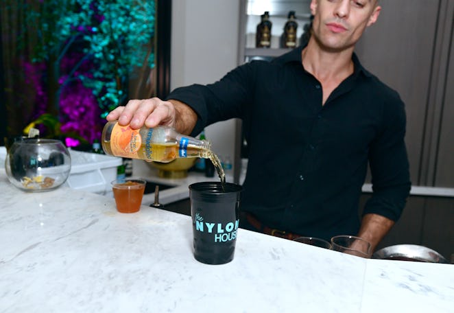 A waiter wearing a black shirt, pouring a drink in a black NYLON cup at Art Basel Miami