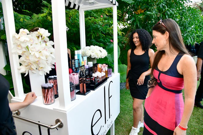 Two women wearing black and pink dresses standing at the ELF stand inside the NYLON house at Art Bas...