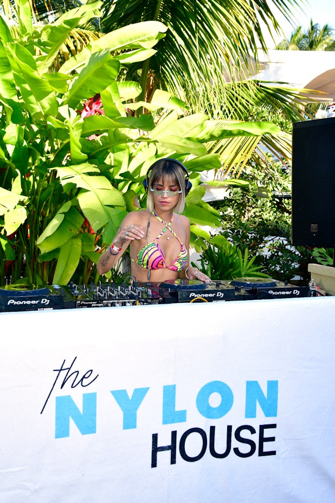 Female DJ standing behind a mixing board inside NYLON house at Art Basel Miami