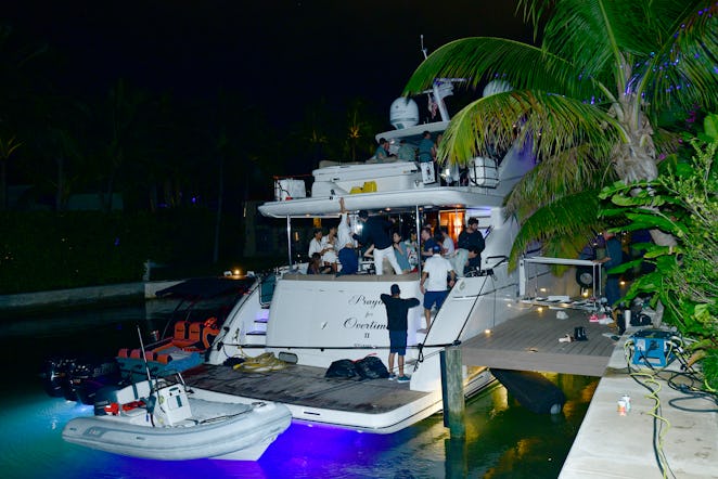 A white yacht next to a pier and palm trees with a lot of people on it at Art Basel Miami