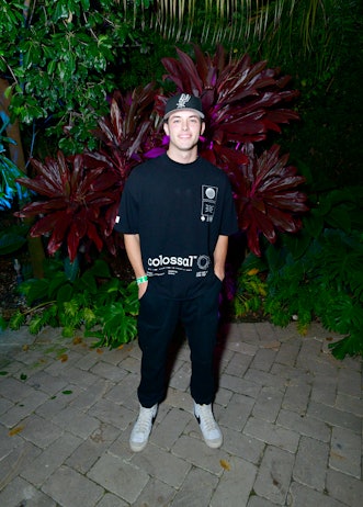 Man wearing a black shirt and pants with a black cap in front of a red plant at Art Basel Miami