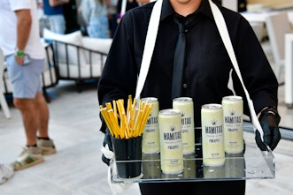 A waiter wearing a black suit and tie carrying beverages inside NYLON house at Art Basel Miami.