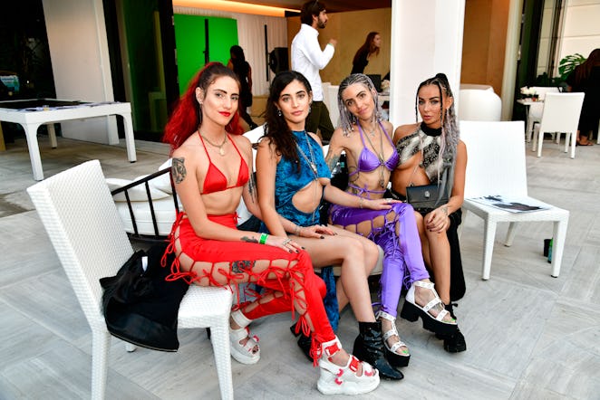 Four women wearing red, blue, purple, and black clothes while sitting inside the NYLON house at Art ...