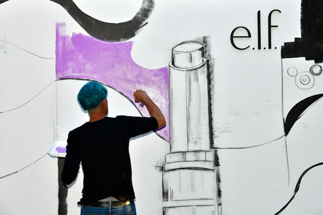 An artist wearing a black shirt, painting an ELF cosmetic mural inside NYLON house at Art Basel Miam...