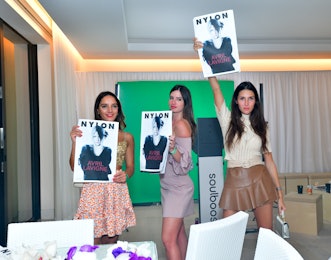 Three women wearing dresses holding photos of Avril Lavigne above their heads inside NYLON house at ...