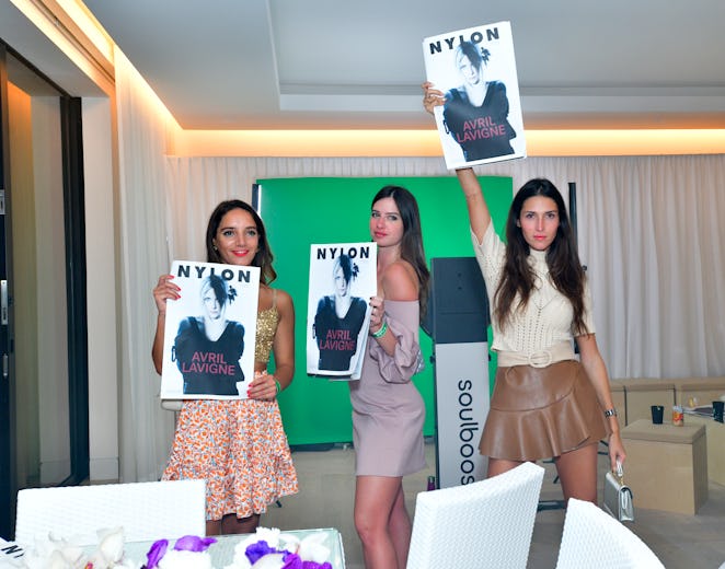 Three women wearing dresses holding photos of Avril Lavigne above their heads inside NYLON house at ...