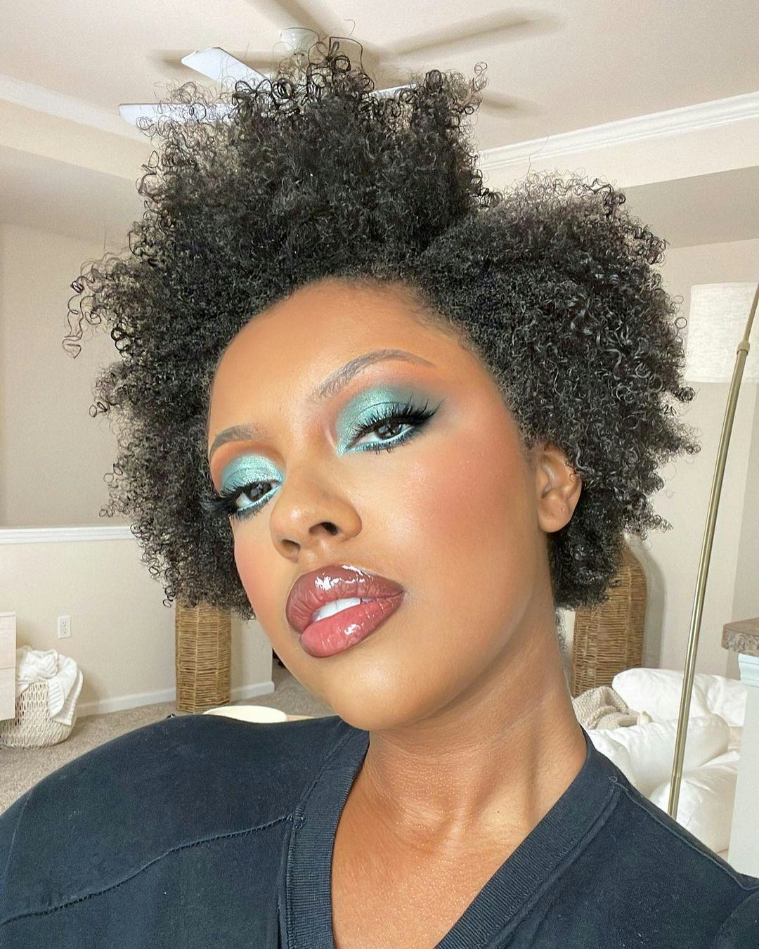 A curly-haired model wearing one of the best cream eyeshadows for effortless application in green
