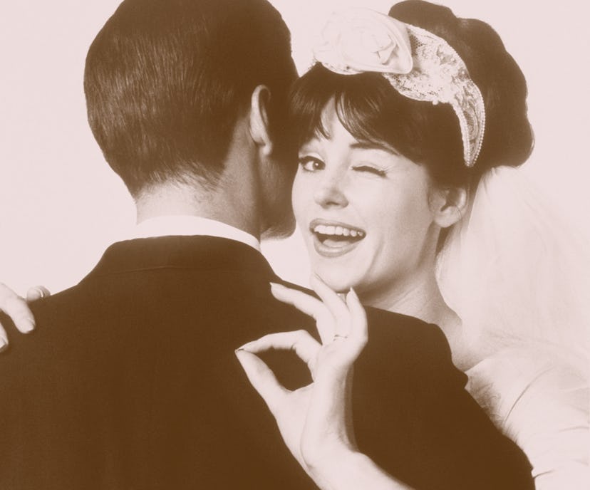 A woman pointing the "okay" hand signal while her partner is hugging her