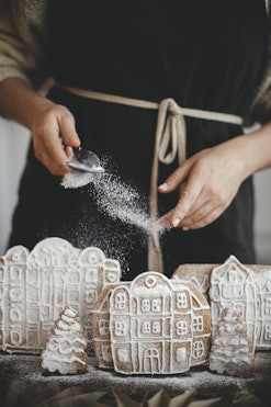 woman sprinkling powdered sugar on gingerbread house village