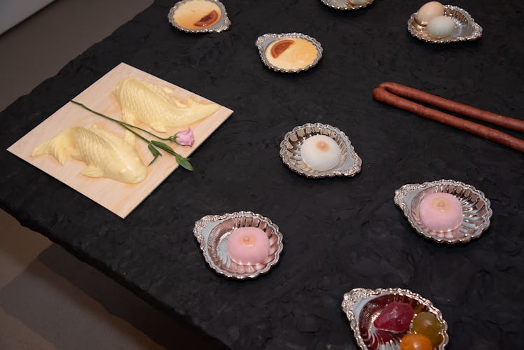 Sugared fruit, fish-shaped butter, and sausages laid out on a black tabletop