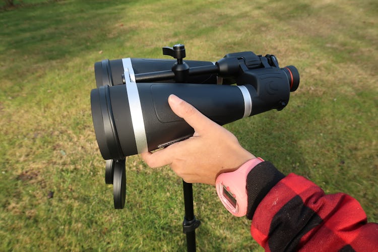 The author has one hand placed around the body of the large binoculars, which sit on a tripod