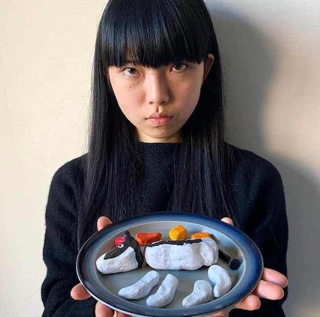 A portrait of Tokyo musician Nana Yamato. She wears a black shirt and holds up a plate with pieces o...
