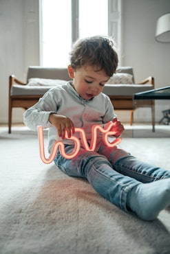 young boy sitting on floor, holding a neon "love" sign