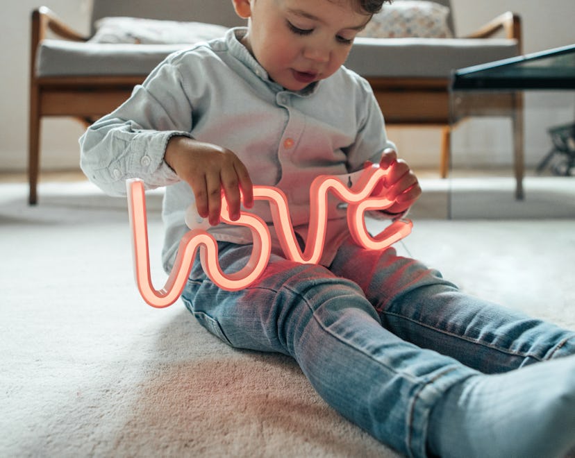 young boy sitting on floor, holding a neon "love" sign