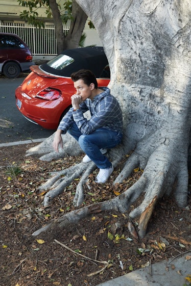 Tom Holland in a grey check shirt, blue denim jeans, and white sneakers, squatting a posing undernea...