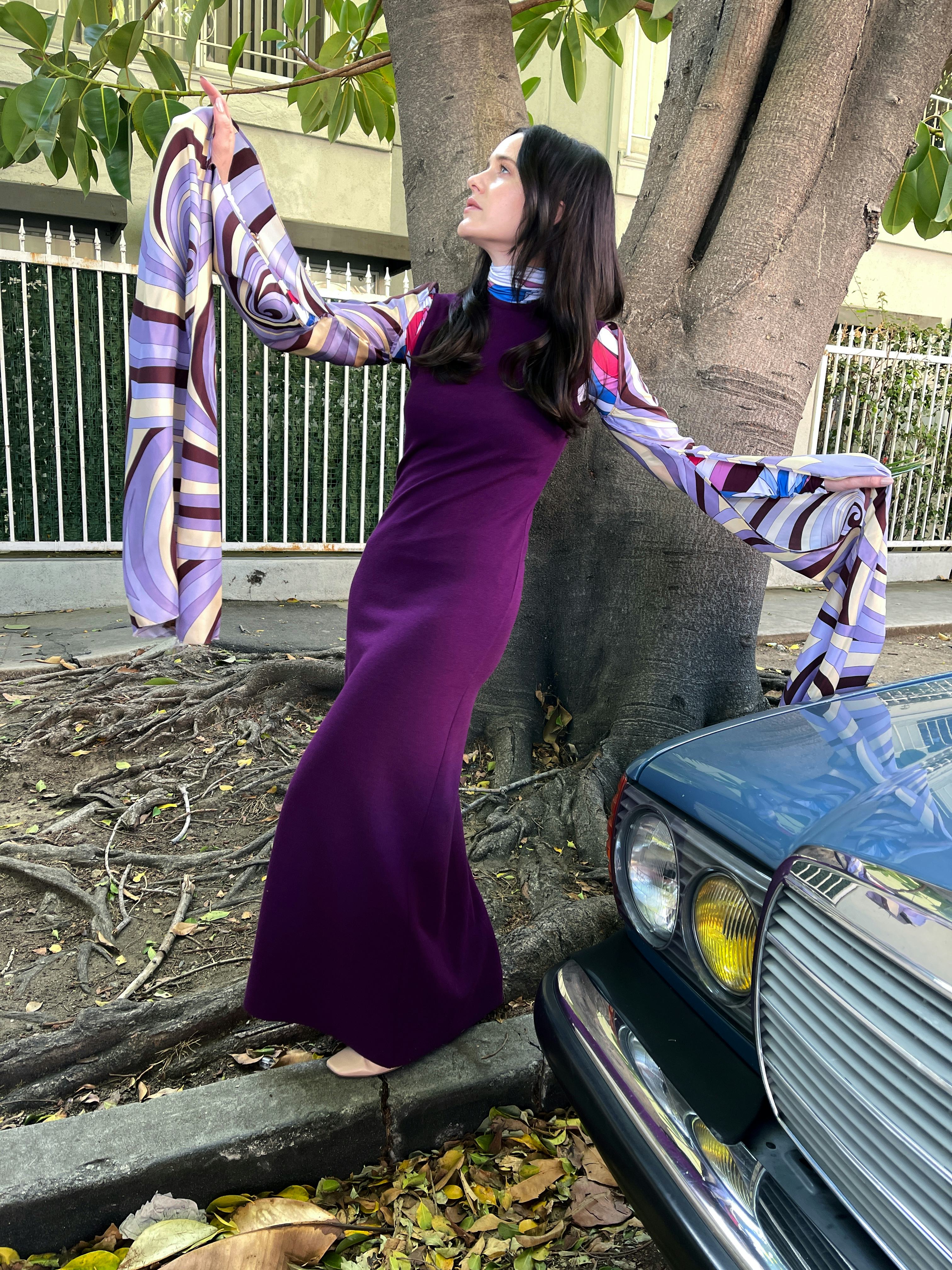 Rachel Brosnahan wears a purple Raf Simons dress and a  turtleneck and posing next to a tree