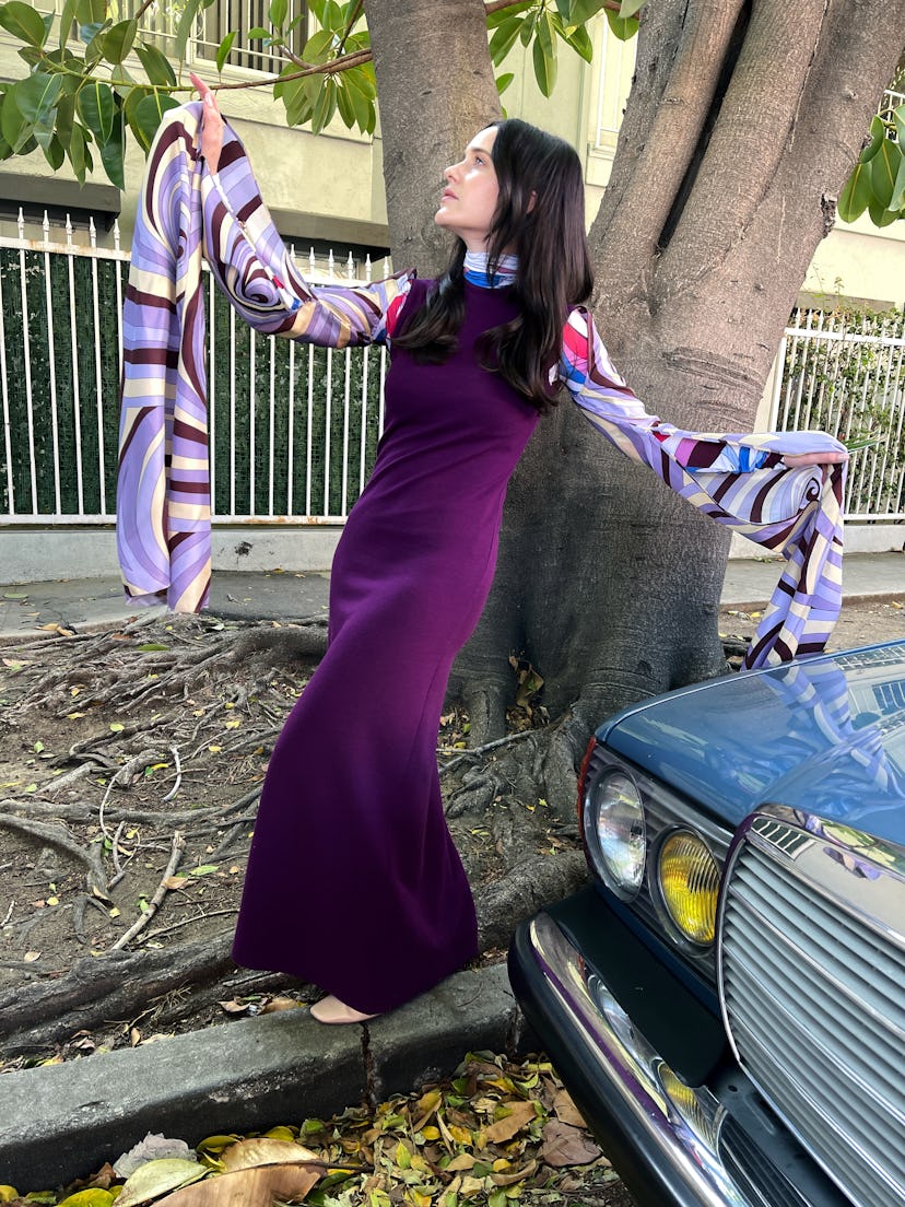 Rachel Brosnahan wears a purple Raf Simons dress and a  turtleneck and posing next to a tree