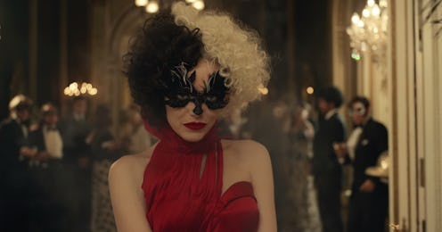 Emma Stone as Cruella in Disney's Cruella, wearing a red halter dress with a black eye mask and blac...