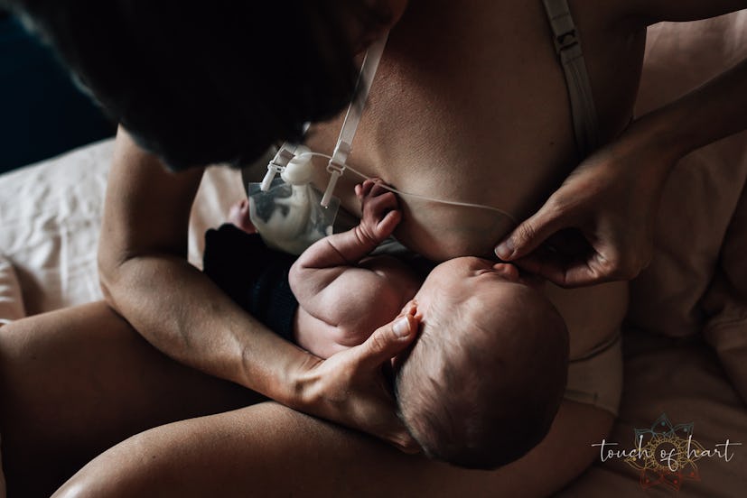 A woman holds one of her nipples and a tube from a supplemental nursing system to a newborn child's ...