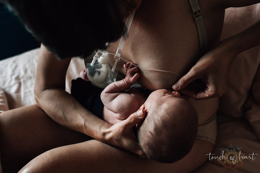 A woman holds one of her nipples and a tube from a supplemental nursing system to a newborn child's ...