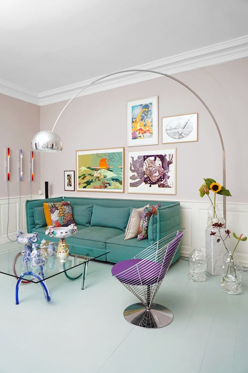 A living room with a green couch, glass table, long overhead lamp and purple chair