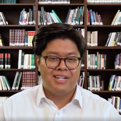 An Asian man sits in front a fake bookshelf background in BR's AI hiring experiment