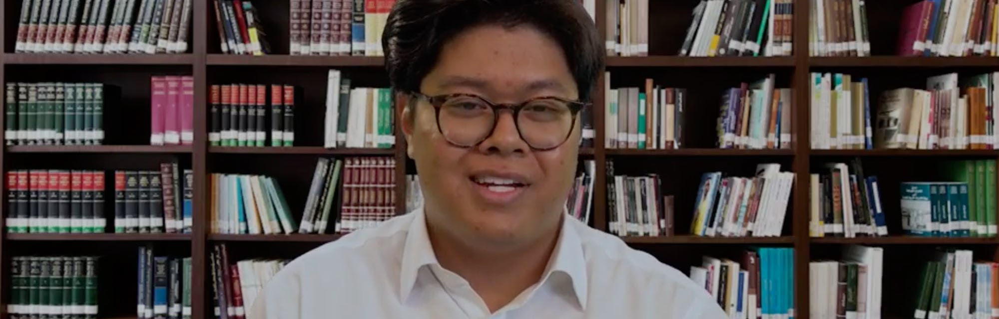 An Asian man sits in front a fake bookshelf background in BR's AI hiring experiment