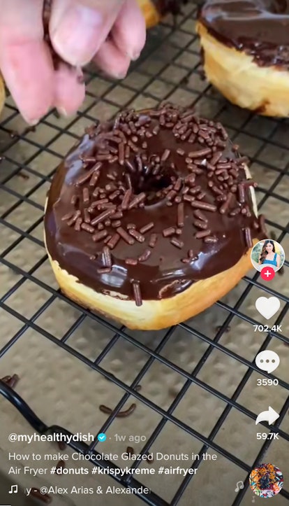 A woman sprinkles chocolate sprinkles on her glazed chocolate donut from her air fryer. 