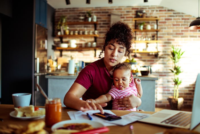 woman punching numbers into calculator while sitting at dining table with infant in her lap