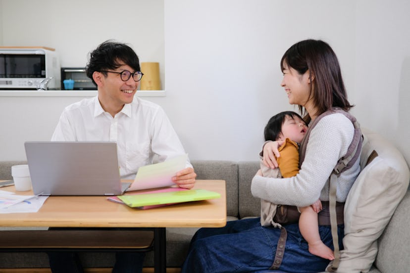 Couple sitting at dining table filling out paperwork with sleeping infant in mother's lap