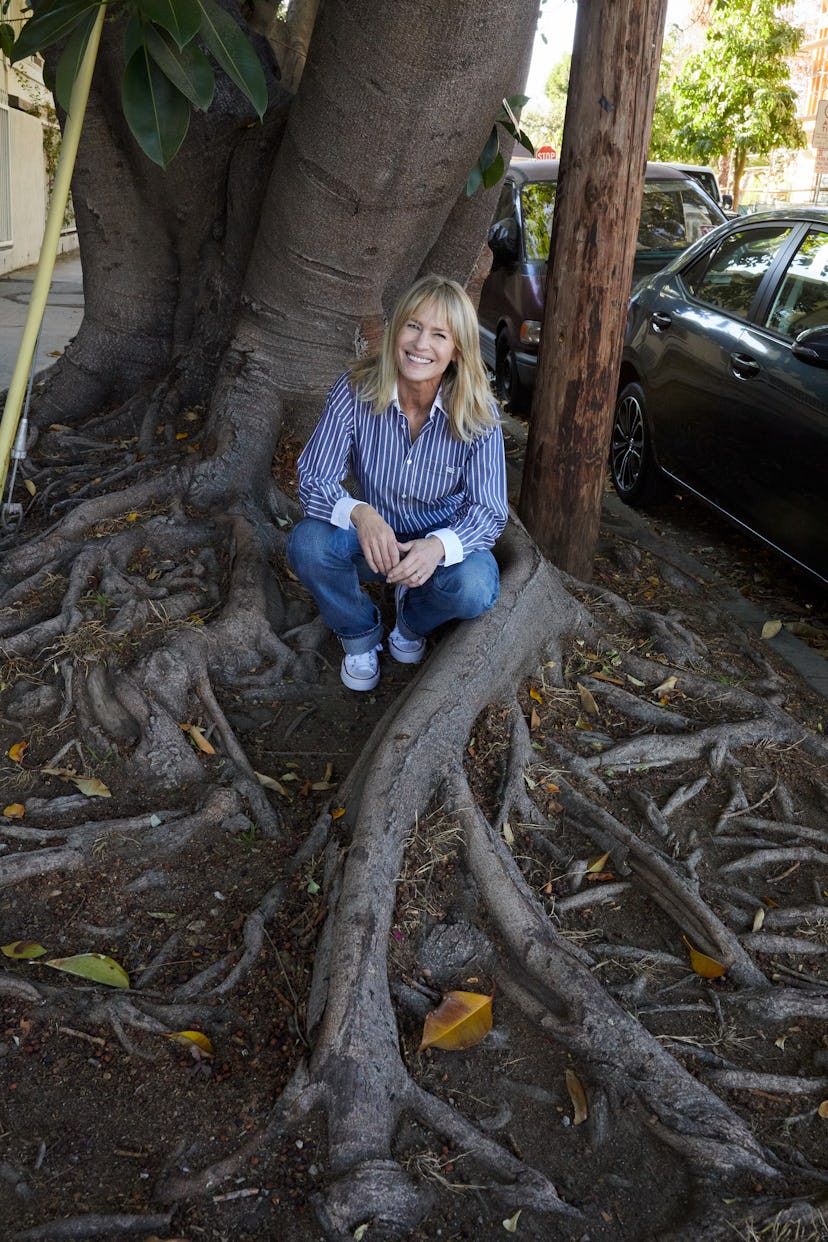 Robin Wright sitting and leaning against a tree in a striped shirt, jeans and white converse