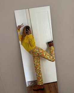 A lady taking a photo of herself in the mirror while wearing yellow patterned pants