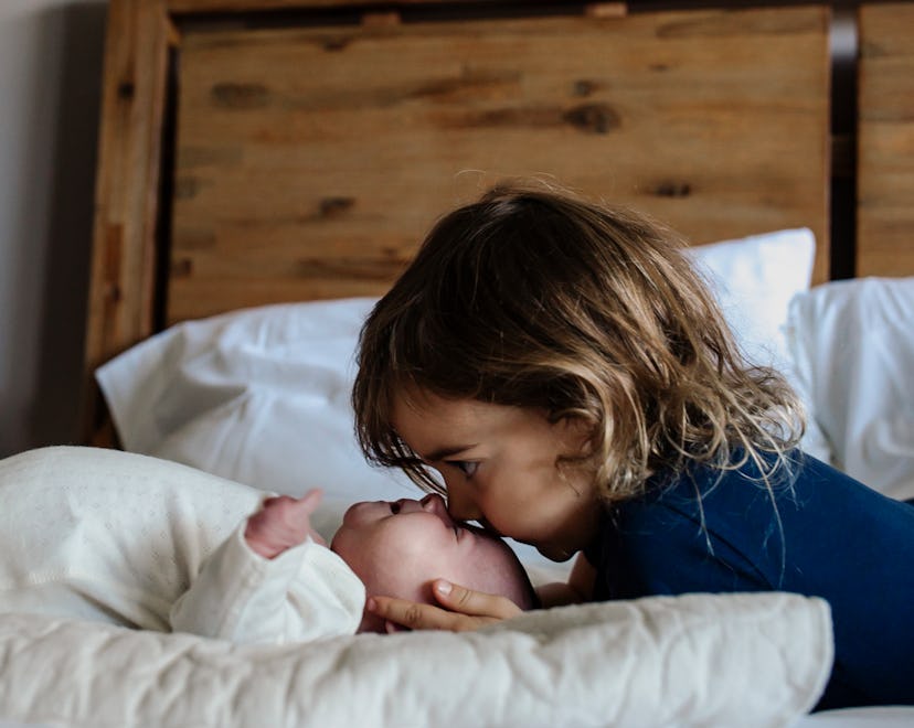 young child kissing newborn sibling on the forehead