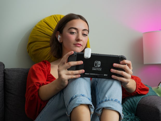 A woman sitting down and playing with a nintendo switch with an audio gadget attached to it