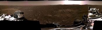 A panoramic view of Mars which includes some parts of the rover with the sun over the horizon